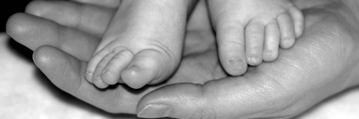 Das Bild ist schwarz/weiß und zeigt zwei Babyfüße auf der Hand eines Erwachsenen