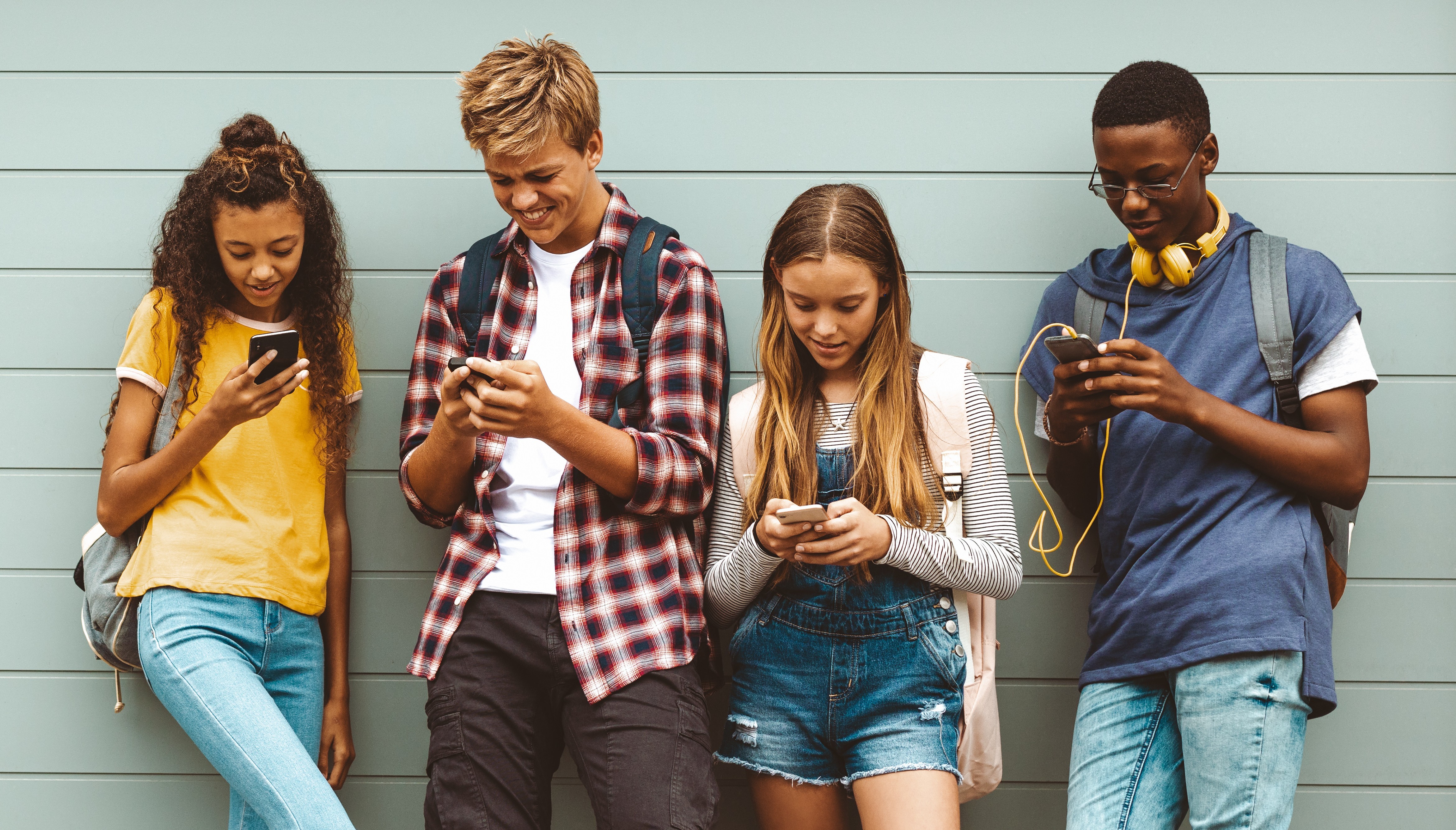 Teenage boys and girls using cell phones standing outdoors