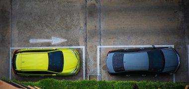 an einer Hecke parken zwei Autos, daneben ist eine Straße