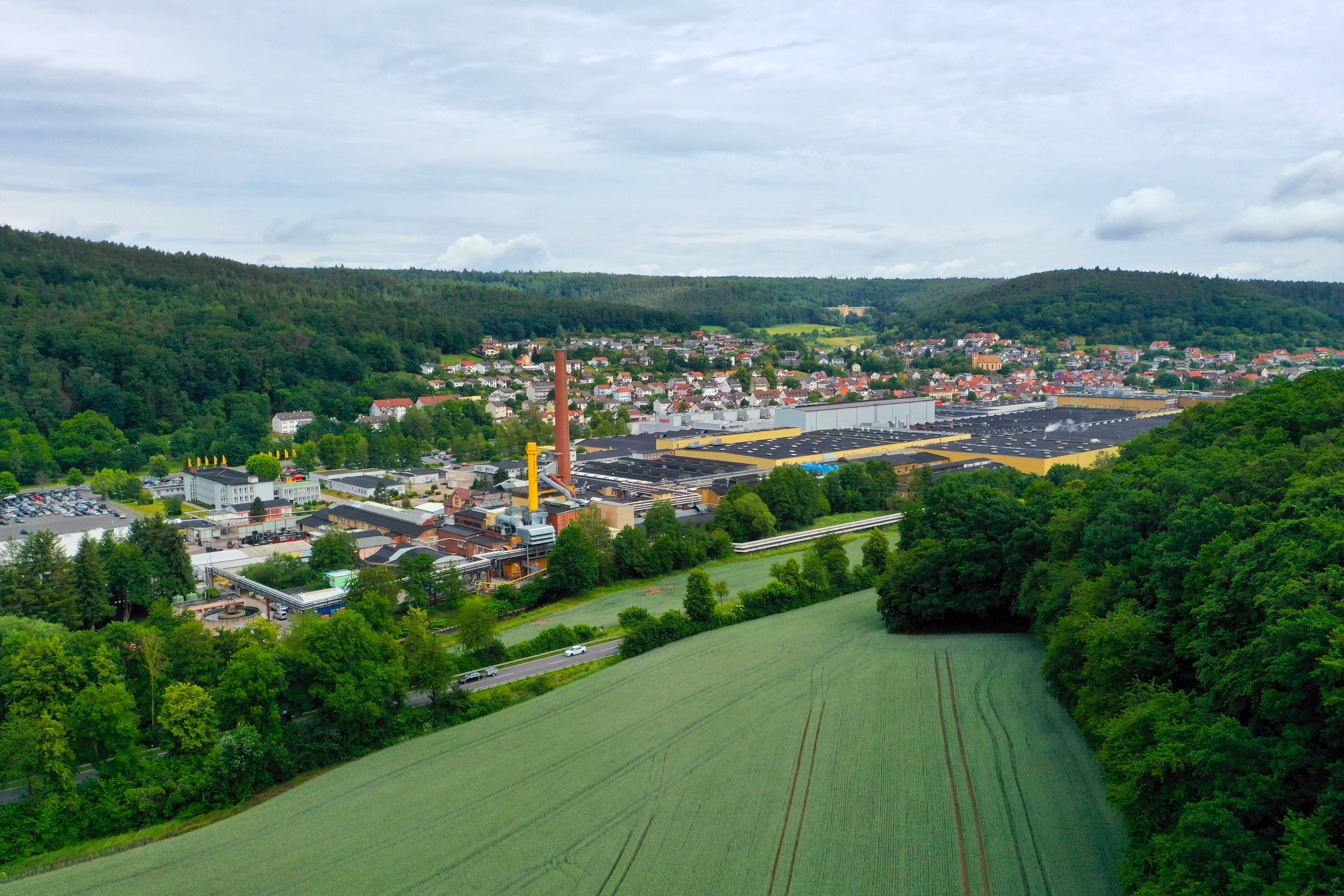 Das Bild zeigt das Fabrikgelände der Pirelli Deutschland GmbH umgeben von Wald und Feld