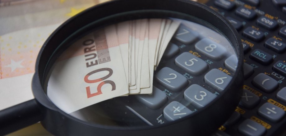 Das Foto zeigt Geldscheine, einen Taschenrechner und eine Lupe und symbolisiert das Thema Haushaltsgenehmigung.