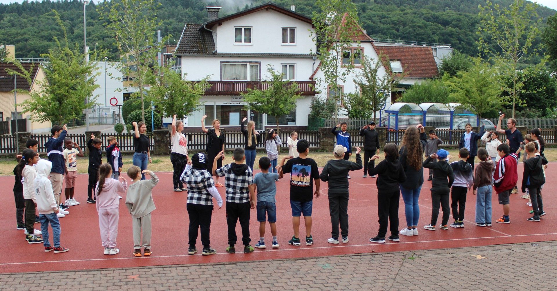 Das Foto zeigt eine Runde mit Kindern auf dem Schulhof in Breuberg-Sandbach und ihren Betreuern bei einem Kursteil zur Sprachförderung.