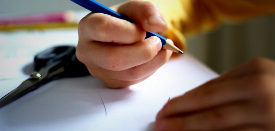 Das Foto zeigt ein Schulkind, das einen Stift in der Hand hält.