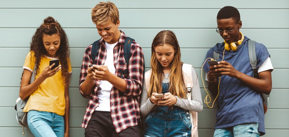 Teenage boys and girls using cell phones standing outdoors Jugendliche schauen in ihr Smartphone